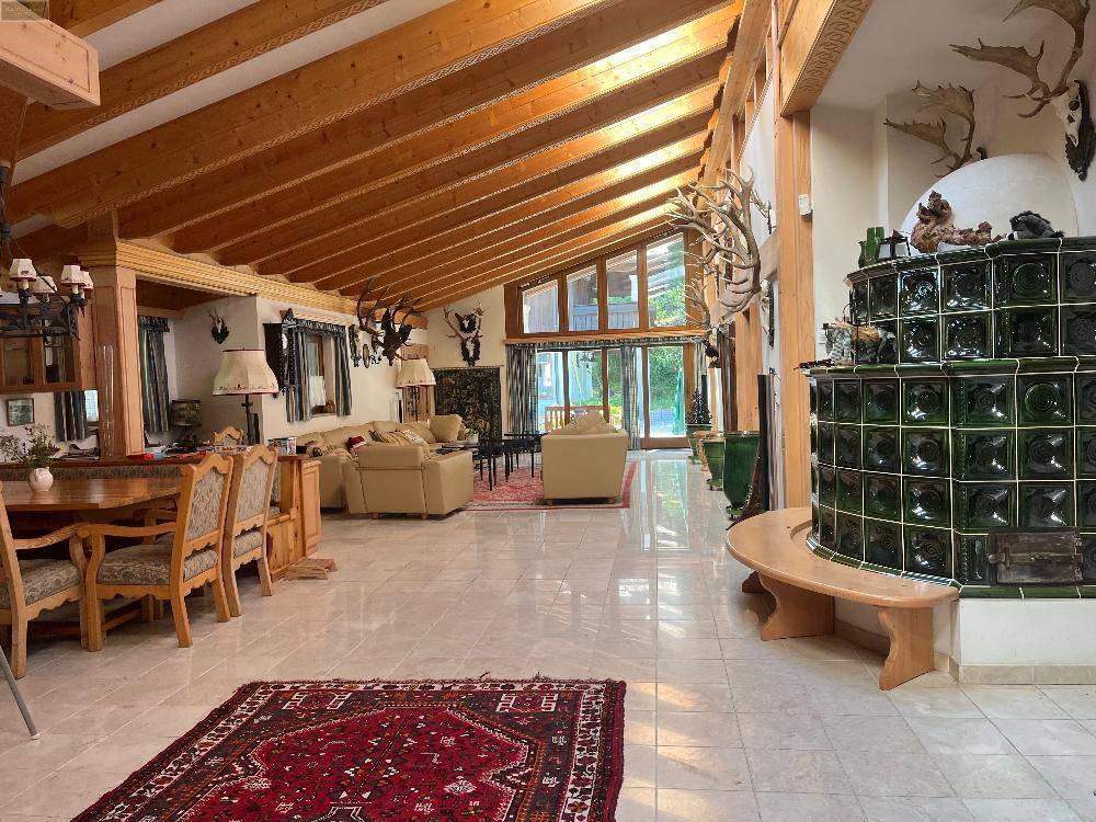 Geräumiger Wohn- und Essbereich mit hohen Holzdecken, Fliesenboden und einem traditionellen Kachelofen.