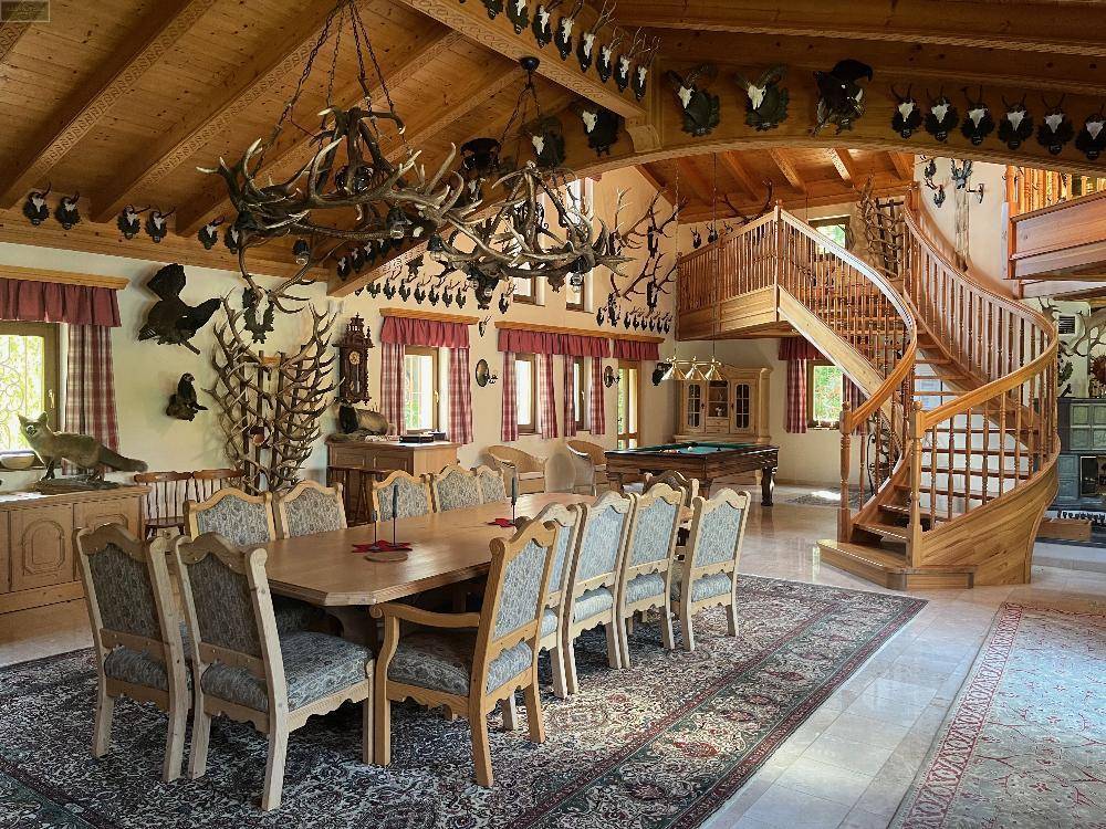 Großzügiger Wohnbereich mit hoher Holzdecke, Billardtisch, Wendeltreppe und zahlreichen Hirschgeweihen als Dekoration.