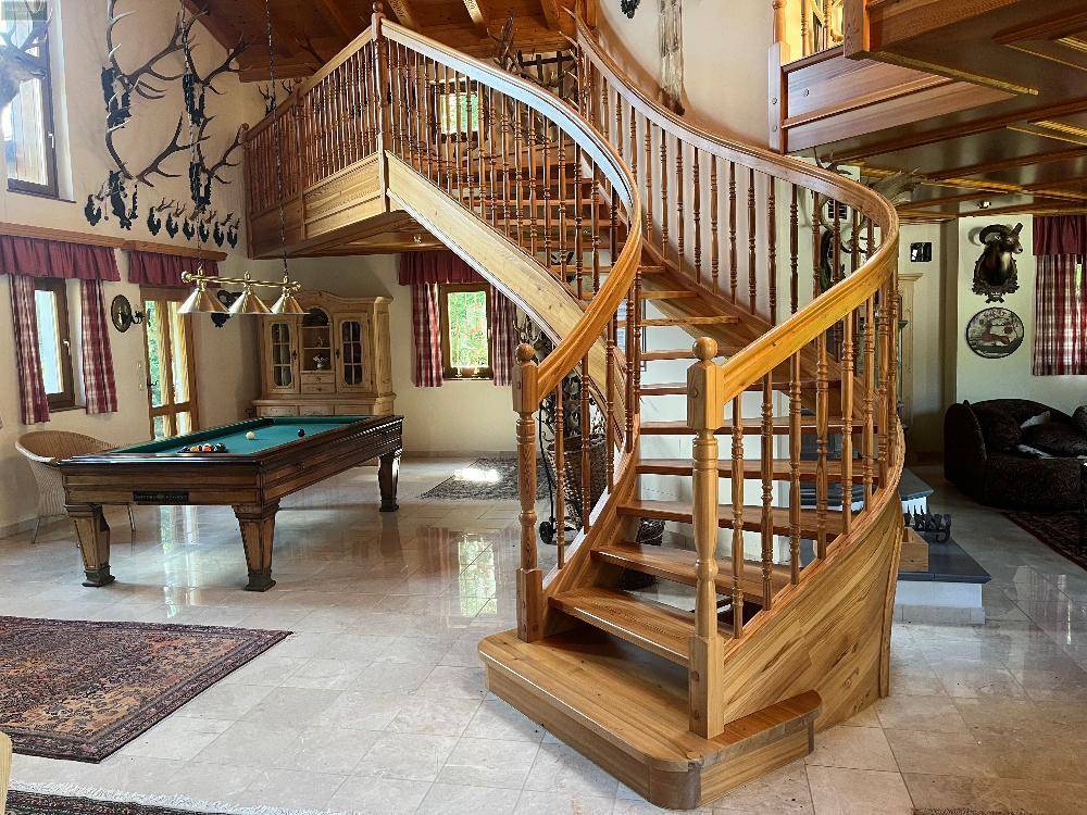 Elegante Holzwendeltreppe führt zu den oberen Etagen, mit einem Billardtisch im Hintergrund des Raumes.