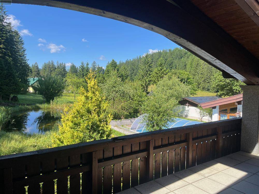 Balkon mit weitem Blick auf den Teich, den Pool und die umliegende grüne Waldlandschaft.