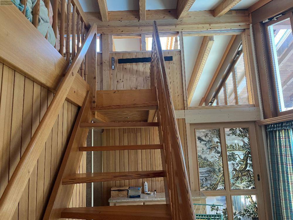 Holztreppe führt zu einem oberen Bereich mit sichtbaren Holzbalken und Holzvertäfelung im traditionellen Stil.