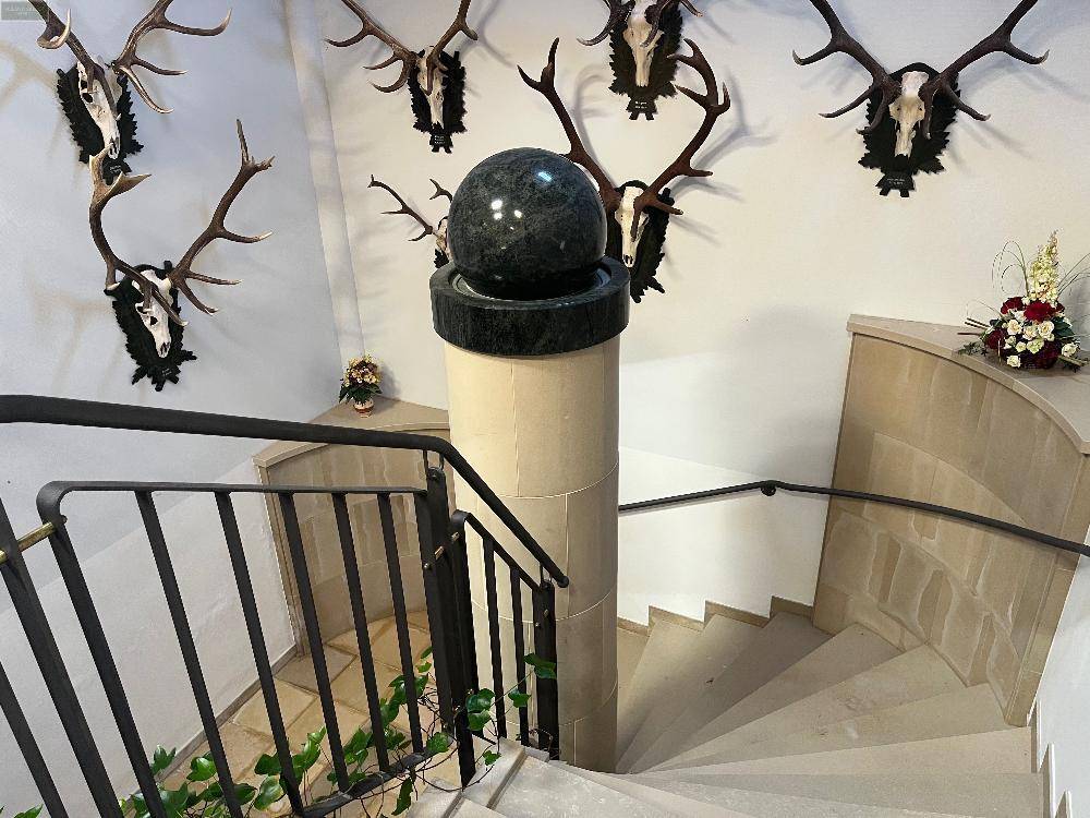 Elegante Wendeltreppe aus Stein mit schmiedeeisernem Geländer und einer dekorativen Kugel auf dem Treppenpfosten.