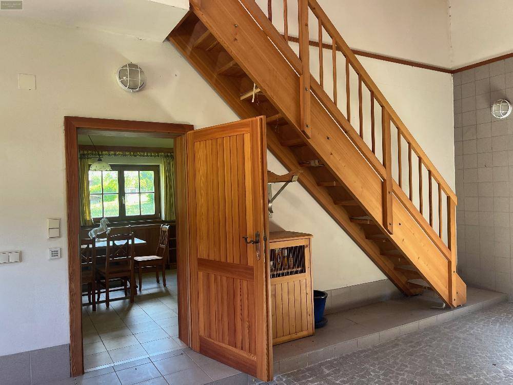Nutzraum mit einer Holztreppe, die zu einem oberen Bereich führt, und einer Tür zu einem weiteren Zimmer.