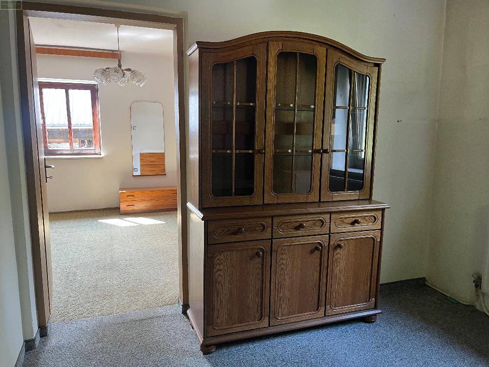 Flur mit Teppichboden und einem klassischen Holzschrank, der den Blick in ein weiteres Zimmer freigibt.