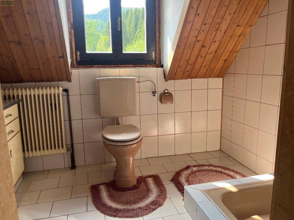 Badezimmer im Dachgeschoss mit beigefarbenem WC, weißen Fliesen und Holzverkleidung an der schrägen Decke.