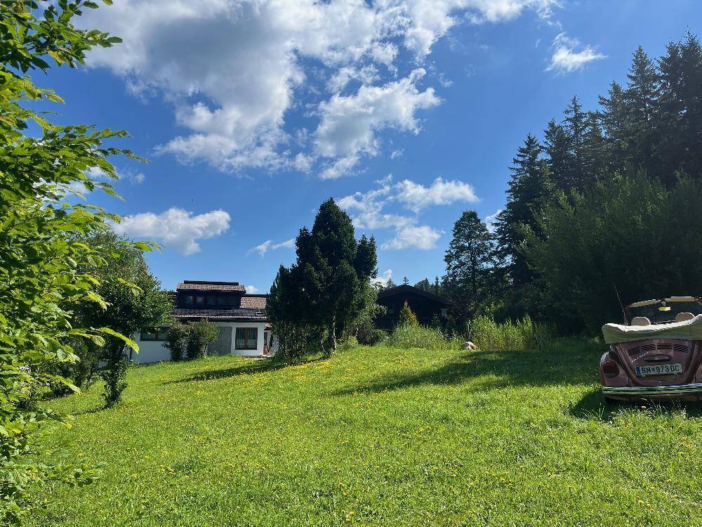 Weitläufige grüne Wiese mit einem Oldtimer und dem Anwesen im Hintergrund unter blauem Himmel.