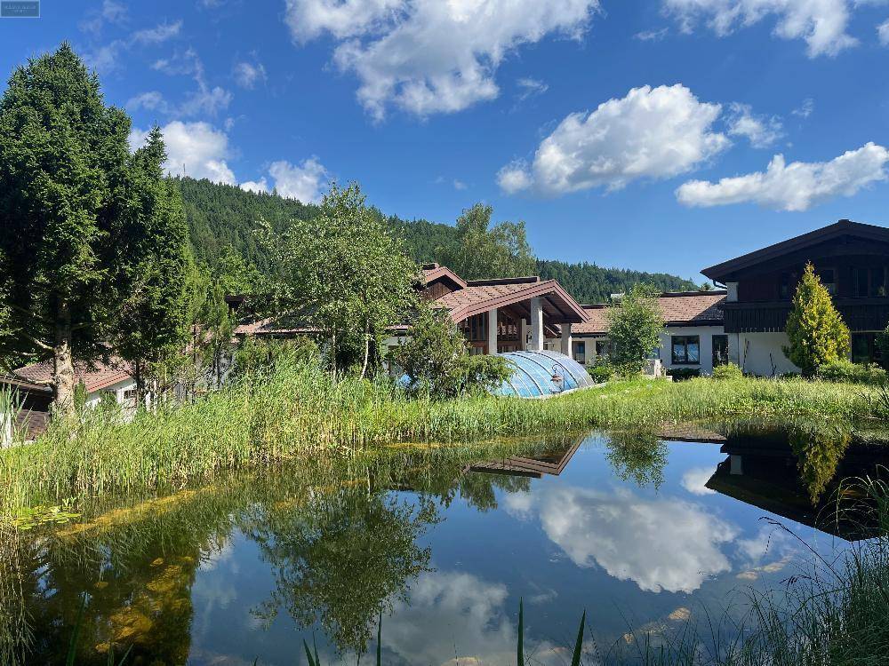 Anwesen mit einem ruhigen Teich im Vordergrund, der den blauen Himmel und die Wolken widerspiegelt.