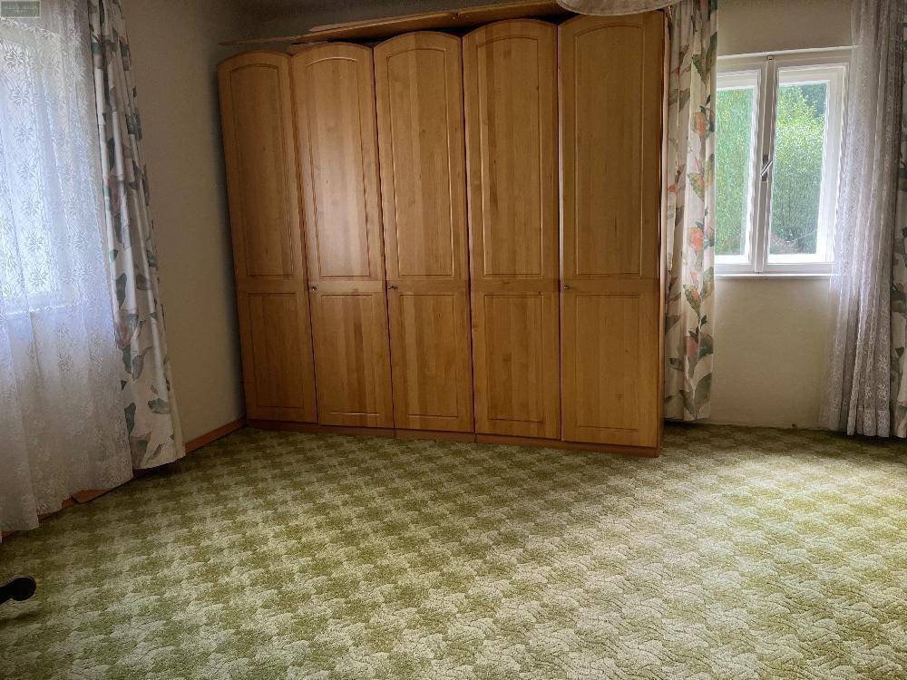 Schlafzimmer mit gemustertem Teppichboden, großen Holzschränken und Blick ins Grüne durch das Fenster.