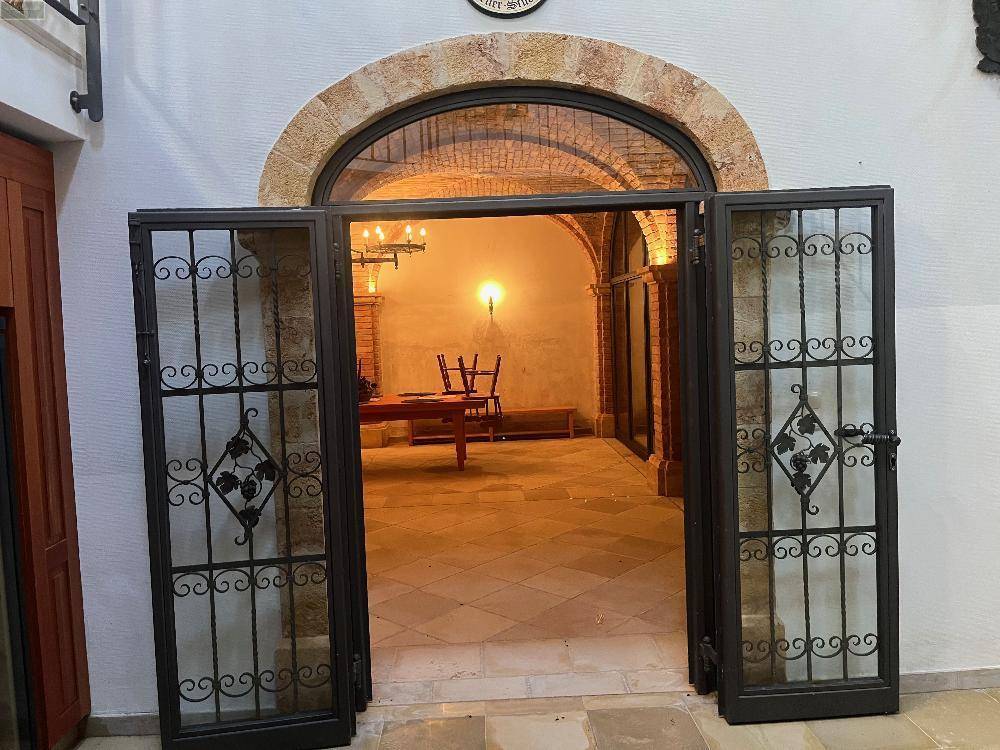 Großer Rundbogen mit kunstvollen Metalltüren, der in einen geräumigen, traditionell gestalteten Raum führt.