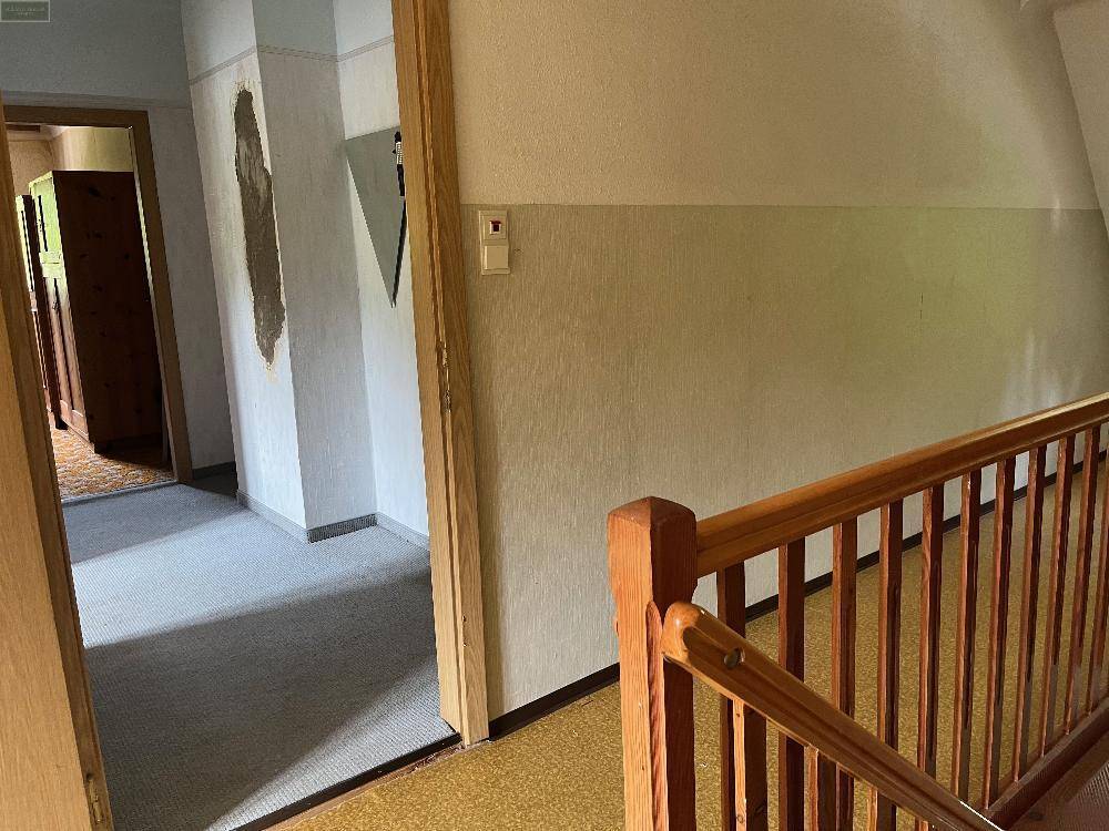 Flur im Obergeschoss mit Holzgeländer und Teppichboden, der zu weiteren Zimmern führt.