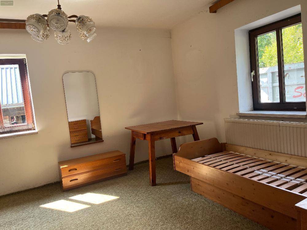 Helles Schlafzimmer mit Teppichboden, einfachem Holzbett und Tisch, sowie einem Spiegel an der Wand.