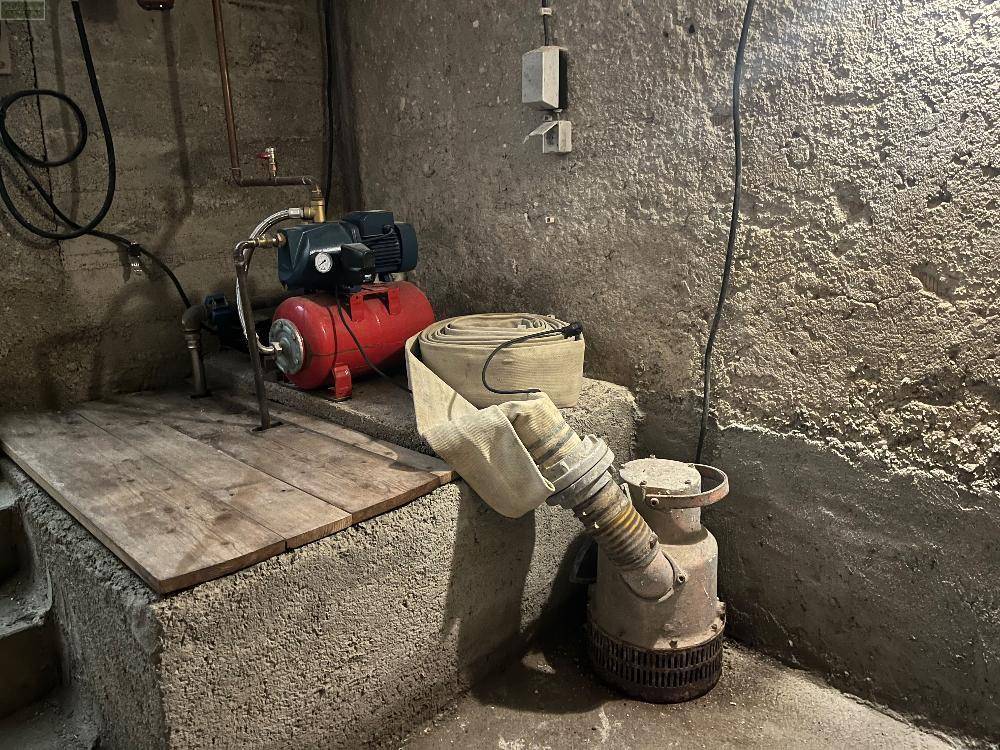 Kellerraum mit Wasserpumpe und Schläuchen, dient als Technik- und Abstellbereich.