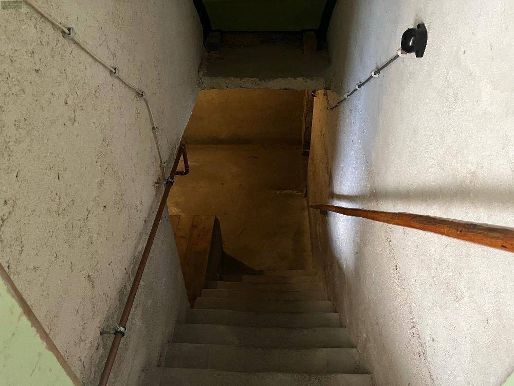 Betontreppe führt in den Keller, mit einfachen Wänden und Handlauf, in rustikalem Zustand.