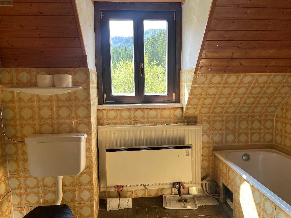 Dachgeschoss-Badezimmer mit gelb-gemusterten Fliesen, Badewanne, WC und Fenster mit Bergblick.