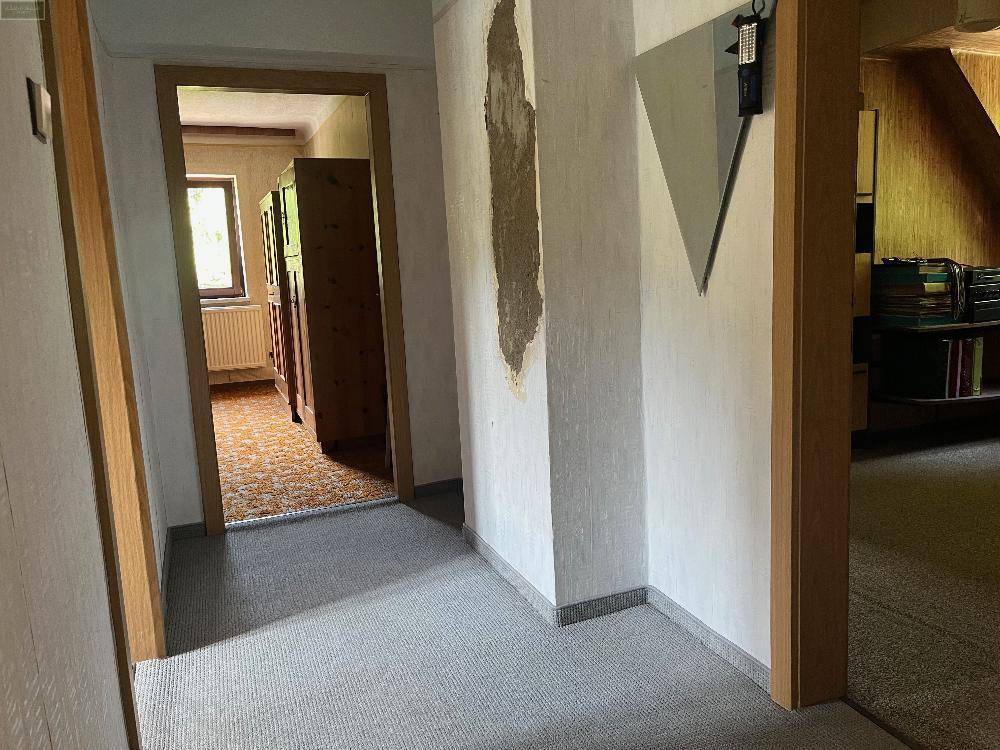 Flur im Obergeschoss mit Teppichboden und sichtbaren Putzschäden an der Wand, renovierungsbedürftig.