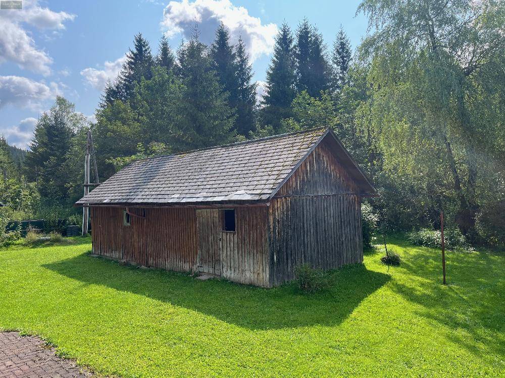 Rustikales Holzgartenhaus mit Satteldach auf einer grünen Wiese, umgeben von Bäumen.