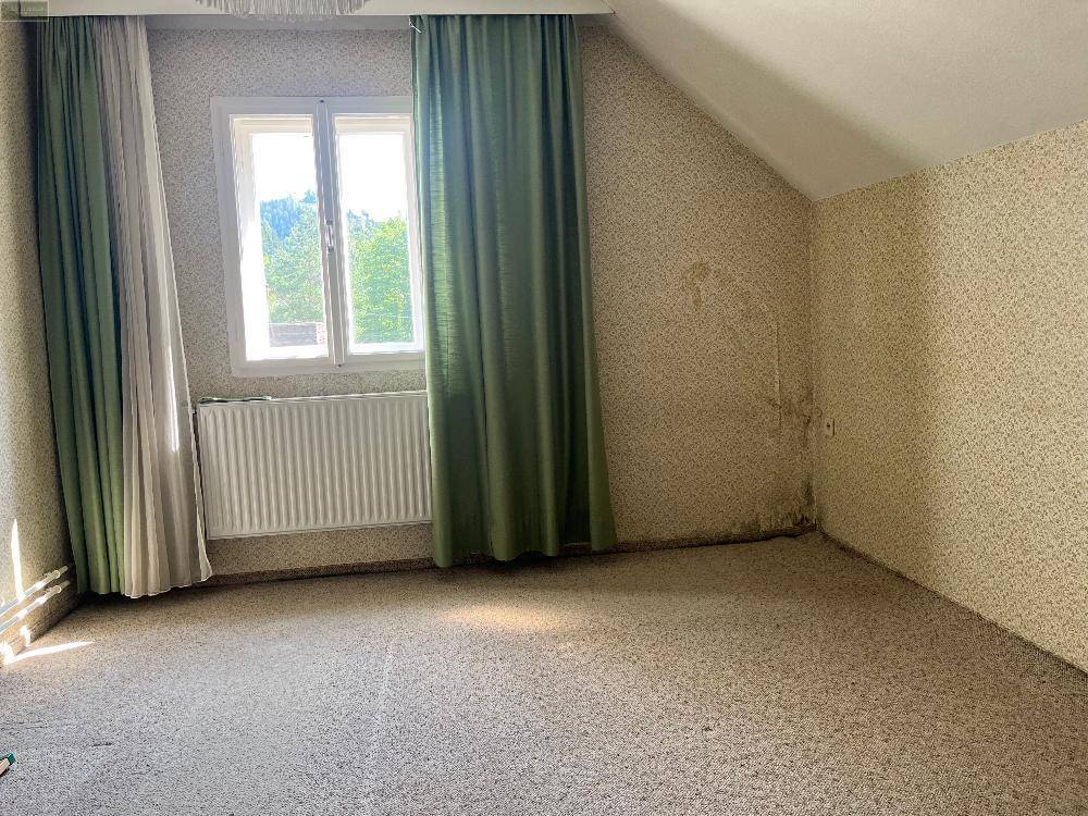 Dachzimmer mit gemusterter Tapete, Teppichboden und Fenster, das viel natürliches Licht hereinlässt.