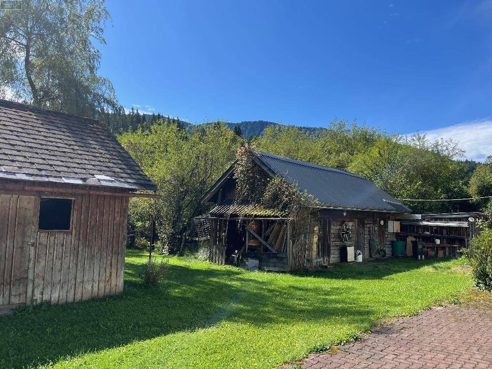 Zwei rustikale Holzschuppen in einem weitläufigen grünen Garten, umgeben von Bäumen und Natur.
