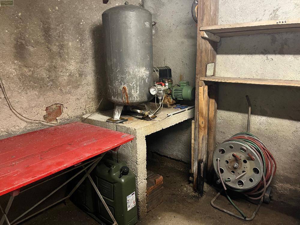 Kellerraum mit großem Wassertank, Regalen und Gartenschlauch, als Lager- und Technikbereich genutzt.