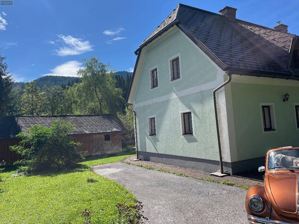 Traditionelles Landhaus mit hellgrüner Fassade und Satteldach, umgeben von Natur und einer Auffahrt.