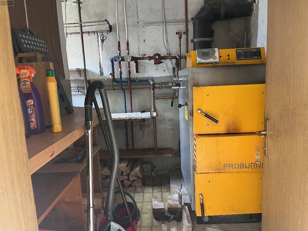 Heizraum mit einem Holzvergaserofen und sichtbaren Rohren, sowie Lagerplatz für Brennholz.