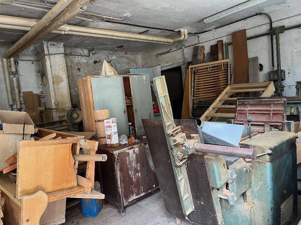 Unaufgeräumter Werkstattraum mit verschiedenen Maschinen, Werkzeugen und Baumaterialien.
