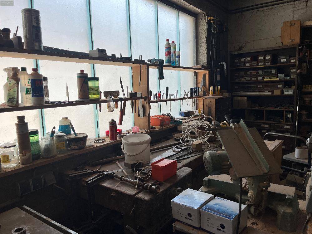 Werkstattbereich mit Werkbank, Werkzeugen und großen Fenstern für Tageslicht.