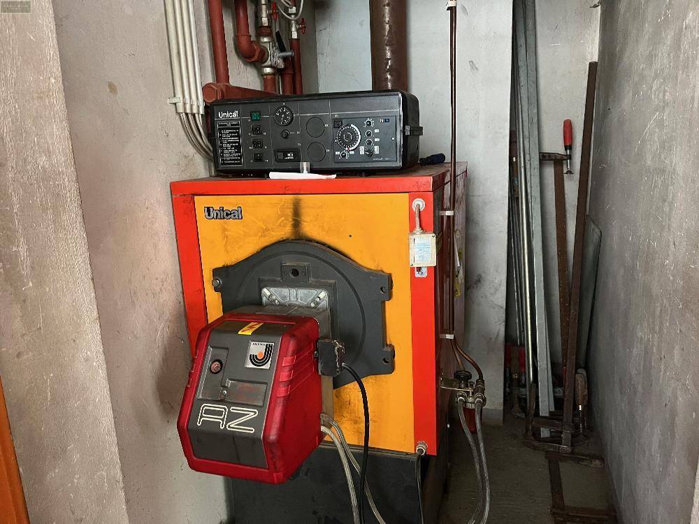 Heizungsraum mit einem älteren Heizkessel und sichtbaren Rohren.