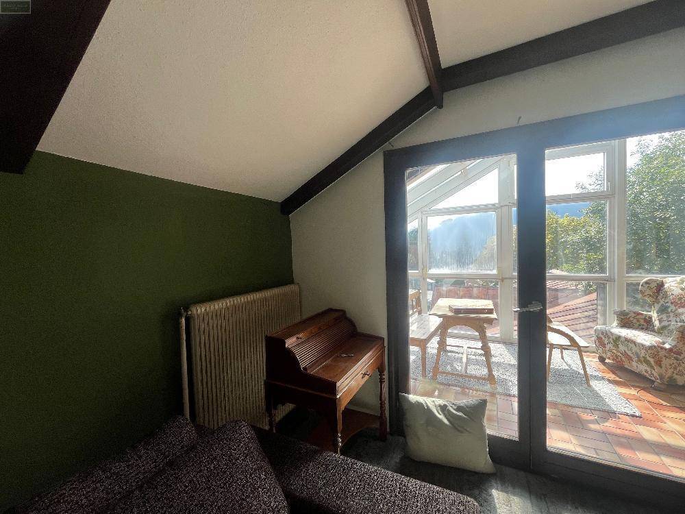 Heller Innenraum mit Dachschräge und Zugang zum sonnigen Wintergarten, der eine Erweiterung des Wohnraums bietet.