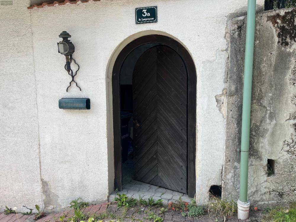 Rustikaler Hauseingang mit Holztür und Hausnummer, umgeben von einer schlichten Fassade.
