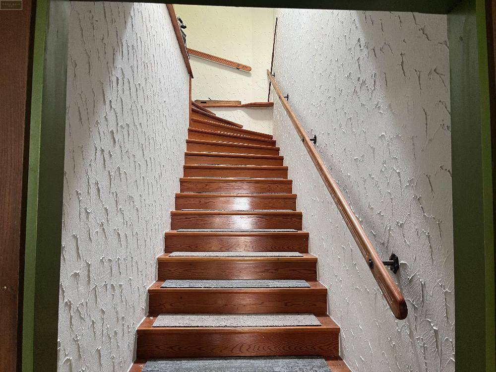 Robuste Holztreppe mit Handlauf und strukturierter Wandgestaltung, die die oberen Etagen verbindet.