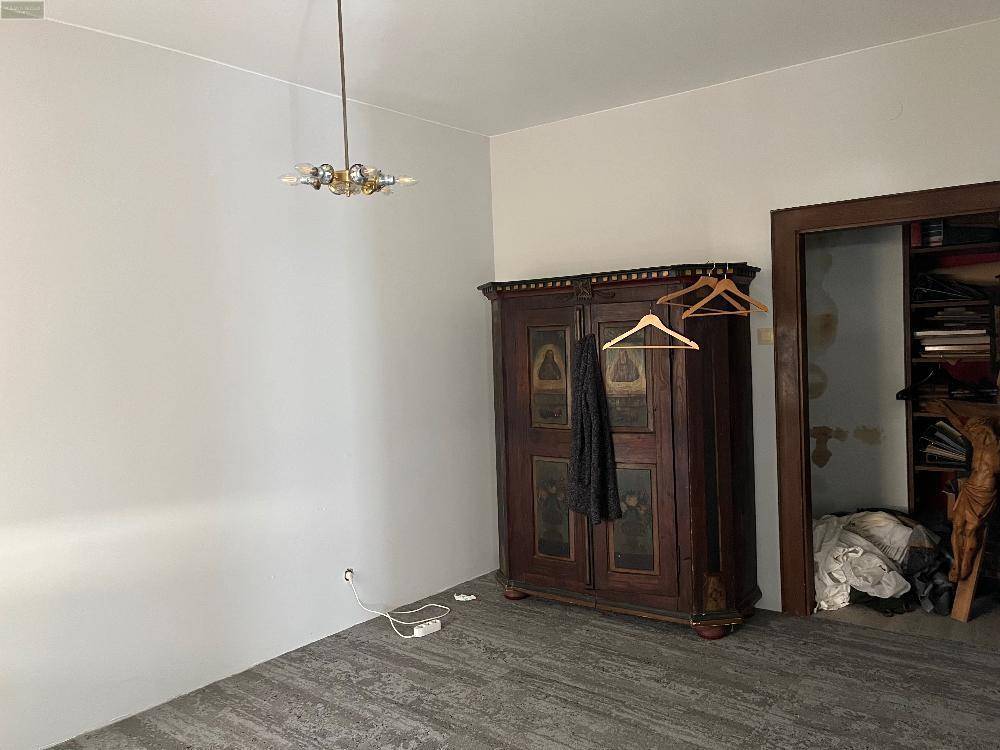 Geräumiges Zimmer mit dunklem Boden und einem antiken Holzschrank, bereit zur individuellen Gestaltung.