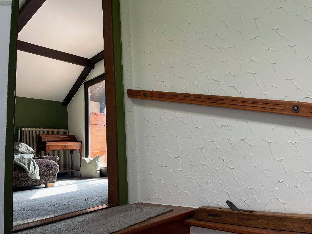 Innenraum mit Dachschräge, Holzbalken und Blick auf den hellen Wintergarten, der zum Verweilen einlädt.