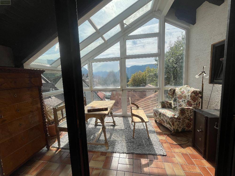 Lichtdurchfluteter Wintergarten mit Bergblick, Terracotta-Boden und Sitzgelegenheiten, perfekt für sonnige Stunden.