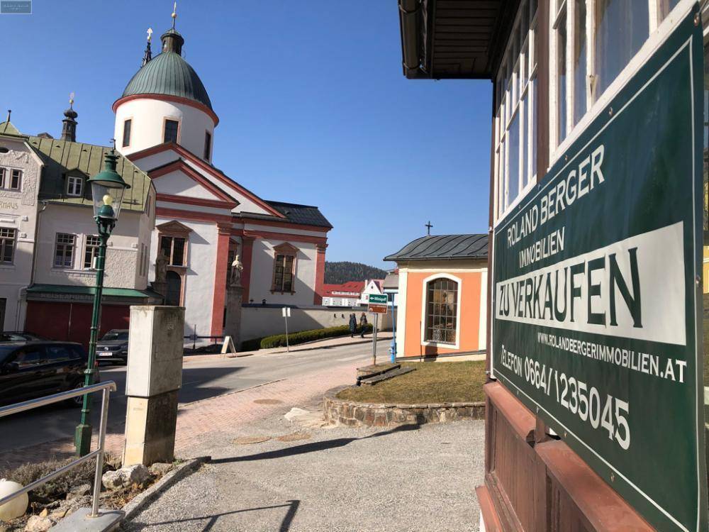 Blick auf eine belebte Straße mit einer historischen Kirche im Hintergrund und einem Verkaufsschild.