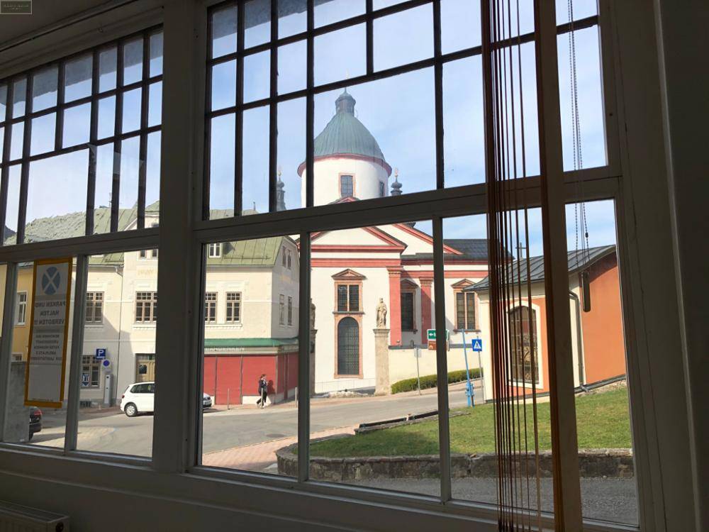 Heller Innenraum mit Blick durch die Fenster auf eine historische Kirche und die Stadtkulisse.