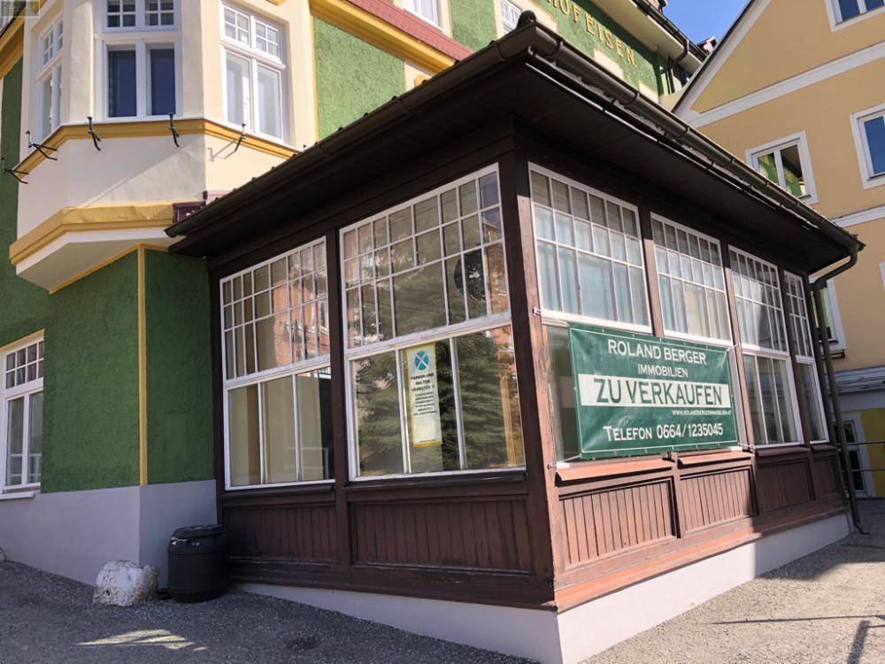 Angebauter Wintergarten oder Veranda mit vielen Fenstern und einem Verkaufsschild an der Fassade.