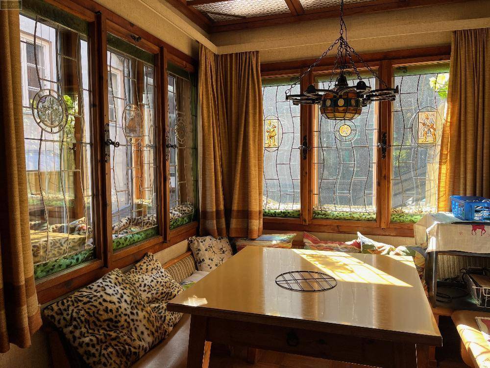 Gemütlicher Wintergarten mit vielen Fenstern, Holztisch und traditioneller Beleuchtung.