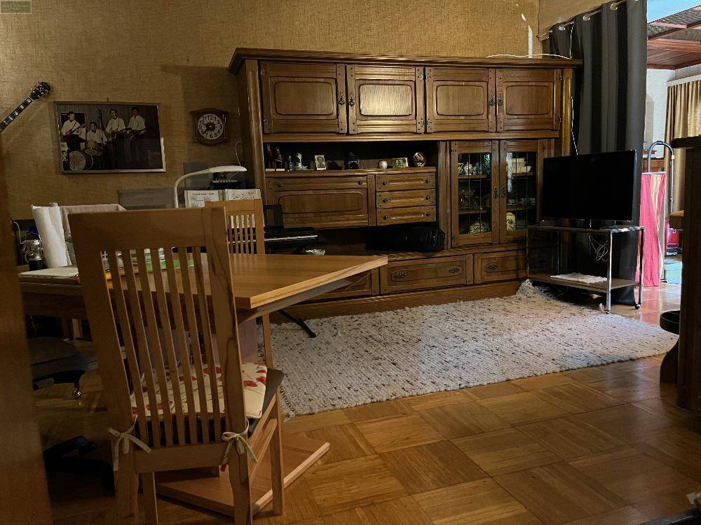 Wohnzimmer mit großem Holzschrank, hellem Teppich und Holzboden.