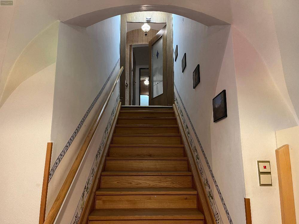 Breiter Treppenaufgang mit Holzstufen, Geländer und gewölbter Decke.