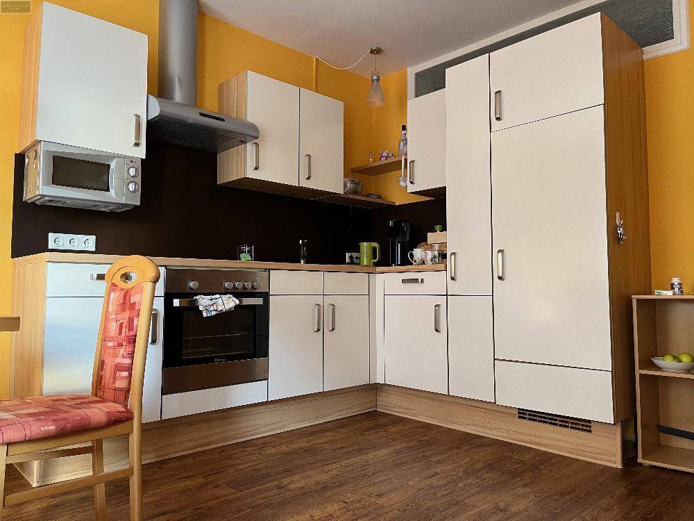 Moderne Einbauküche mit weißen Schränken, Holzboden und gelben Wänden.