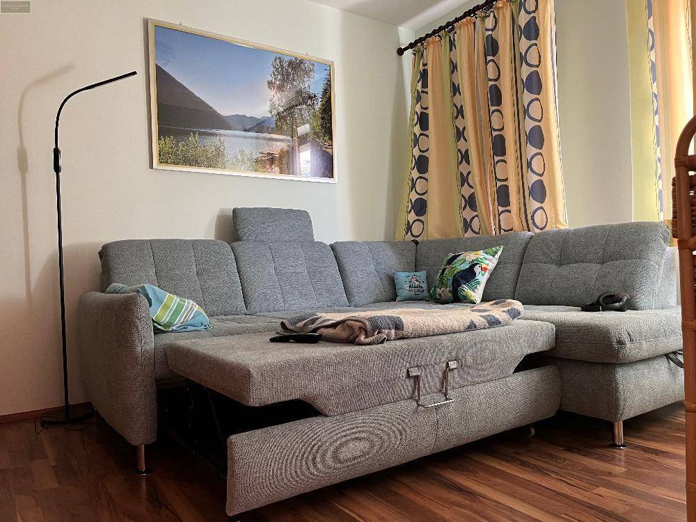 Gemütliches Wohnzimmer mit großem Ecksofa, Holzboden und dekorativen Vorhängen.