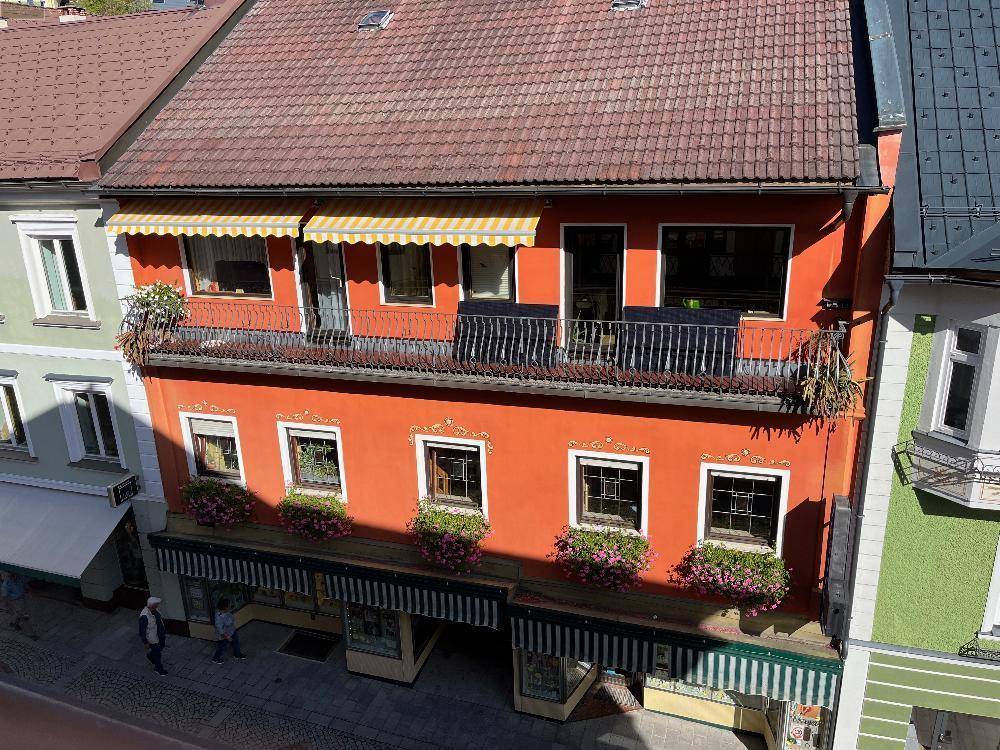 Dachansicht eines Gebäudes mit rotem Ziegeldach, Balkon und gelb-weiß gestreiften Markisen.