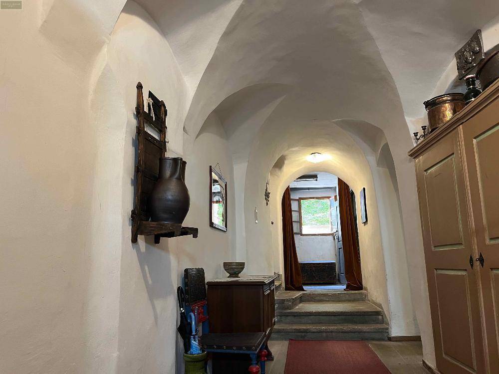 Langer, gewölbter Flur mit rustikalen Möbeln und einem roten Teppich.