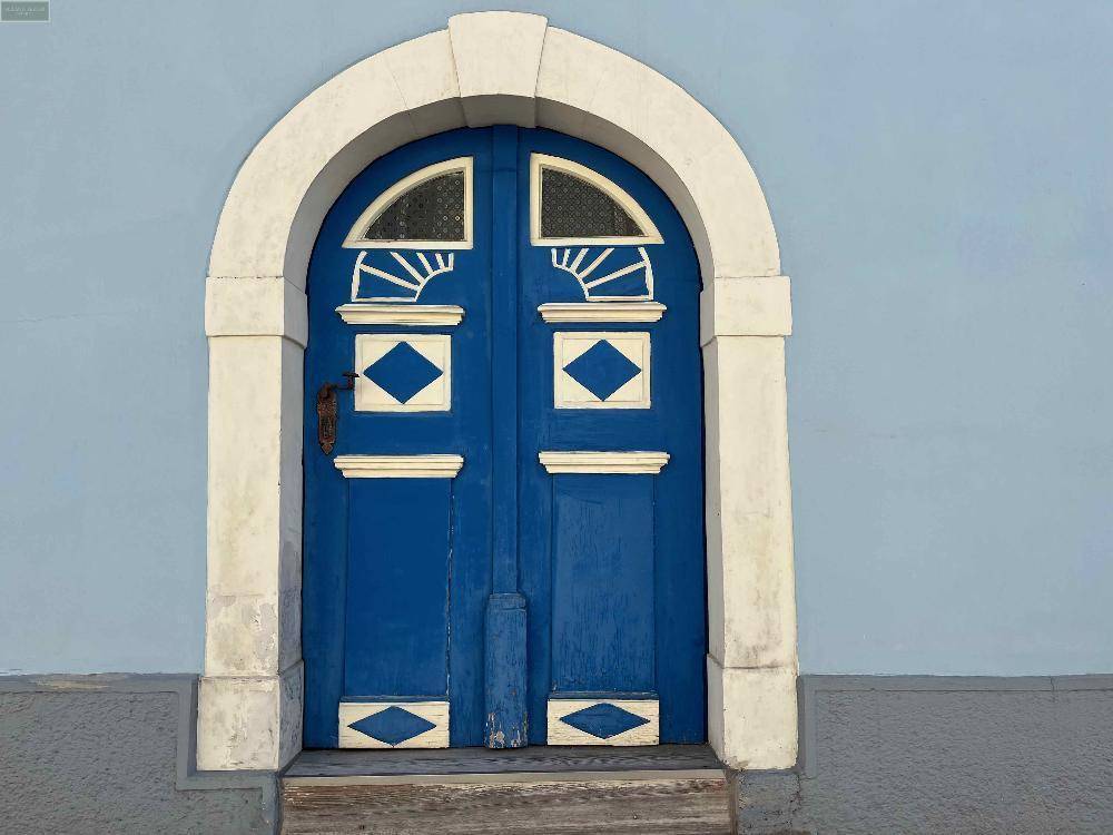 Detailaufnahme einer historischen blauen Eingangstür mit weißem Steinrahmen und dekorativen Elementen.