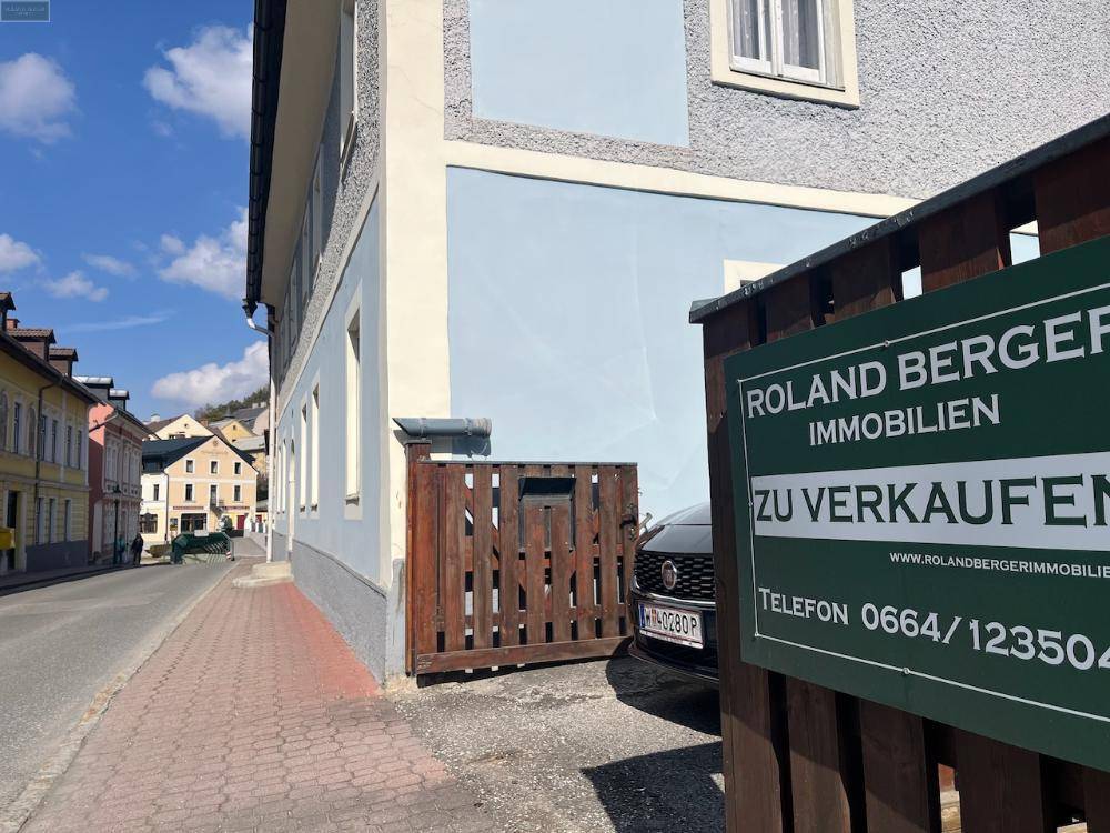 Seitenansicht des Gebäudes mit einem "Zu Verkaufen"-Schild und Blick auf die Straße.