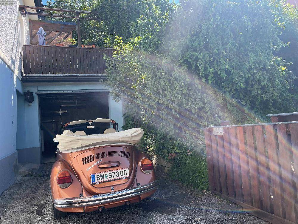 Klassisches Cabrio vor der Garageneinfahrt, umgeben von üppigem Grün.