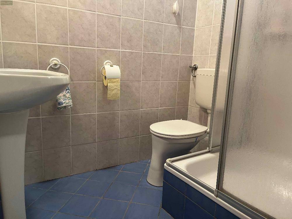 Funktionales Badezimmer mit beigefarbenen Fliesen, Duschkabine und Standwaschbecken.