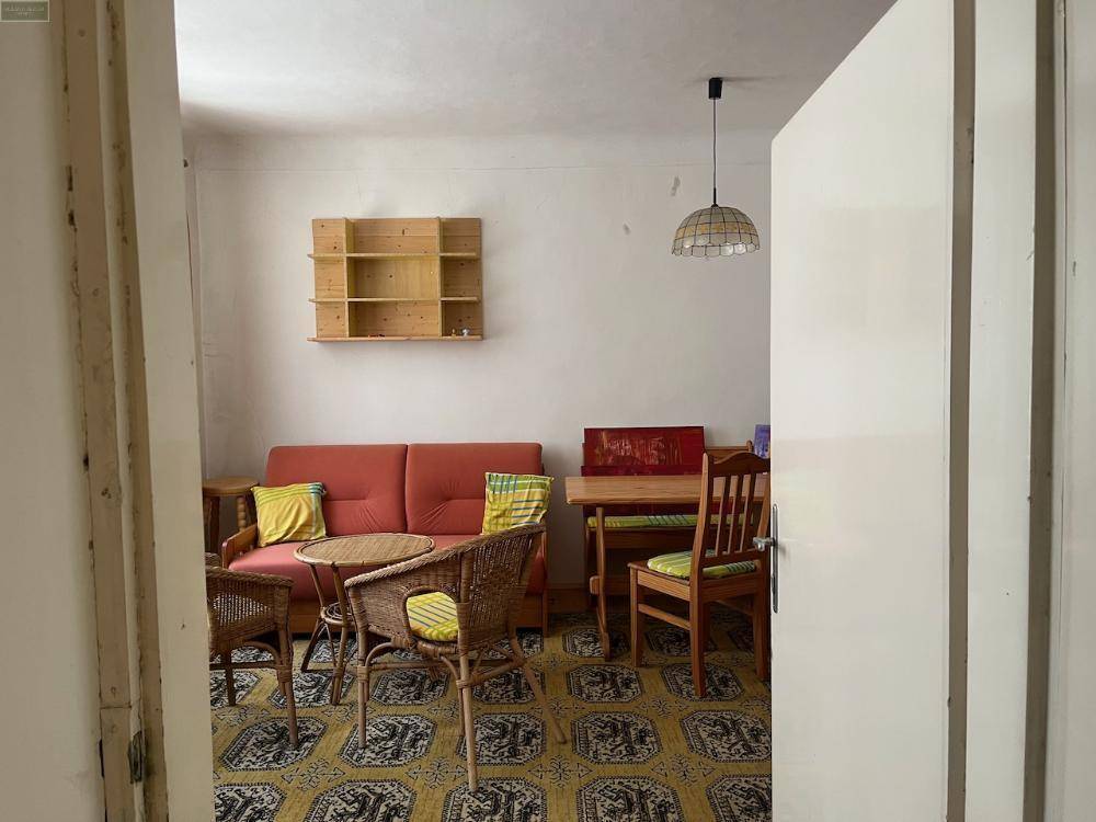 Gemütlicher Wohn- und Essbereich mit Korbmöbeln, Sofa und einem gemusterten Teppich.