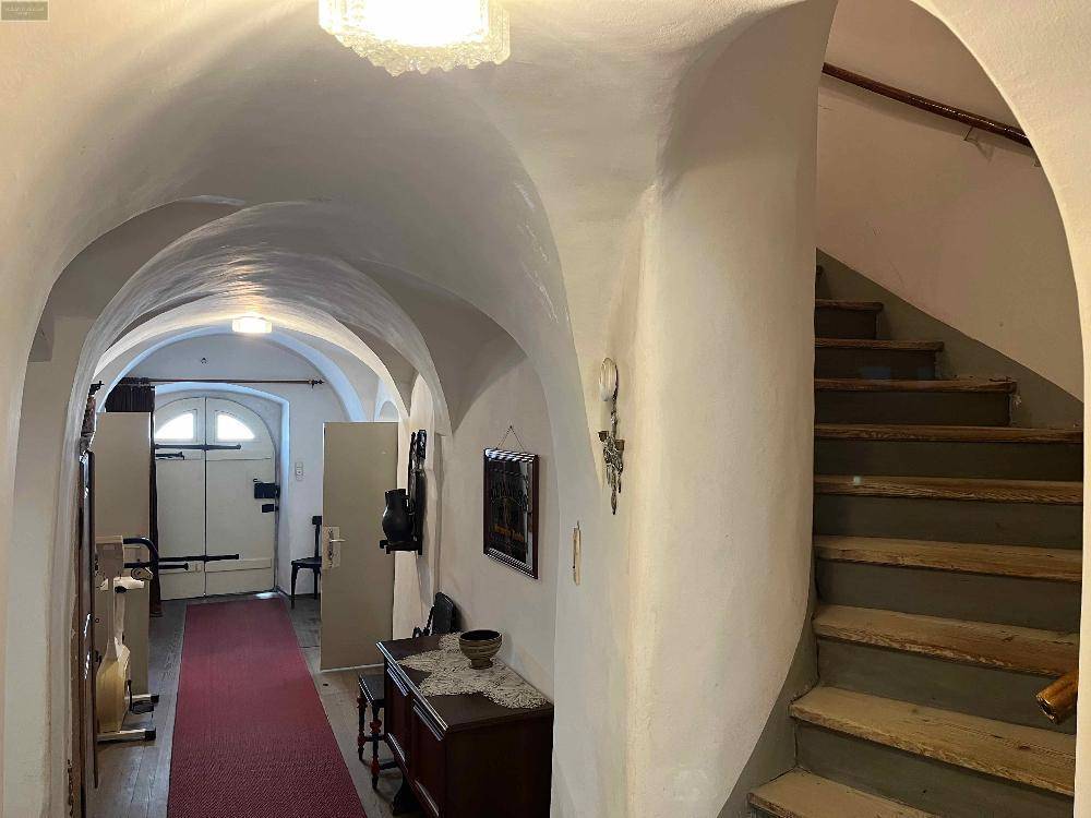 Historischer Flur mit Gewölbedecken und einer Holztreppe, die in die oberen Stockwerke führt.